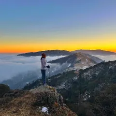 A trekker stands in awe, watching the sun rise over a sea of clouds from the Sandakphu peak. This is the reward after a challenging climb, a moment of pure peace and beauty.