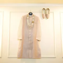 A "getting ready" shot of the groom's wedding attire, featuring his sherwani, 'juttis', and 'mala', all beautifully arranged.