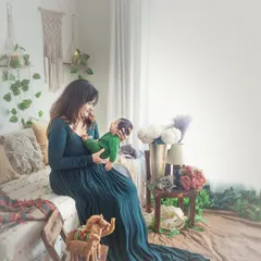 A wider shot of the new mother and her baby in the boho studio. The flowing green dress and the beautifully arranged decor create a stunning, lifestyle-focused newborn portrait that tells a story of new life.