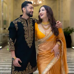 A perfectly coordinated couple. This shot captures Zaid Darbar in our custom black and gold embroidered sherwani, a classic choice for a wedding ceremony or reception that complements his partner's attire beautifully.