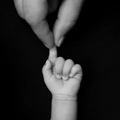 An intimate black and white shot of a parent's finger gently touching their baby's tiny, grasping hand. This image speaks volumes about connection and trust.