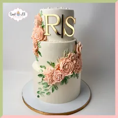 A beautiful three-tiered cake personalized with a gold monogram. The design is adorned with a cascade of delicate, handmade sugar roses in a lovely peach hue, creating a look of timeless romance and elegance.