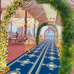 A beautiful outdoor wedding entrance featuring a series of floral and greenery arches over a royal blue carpet. This creates a long, picturesque walkway into the main event area.