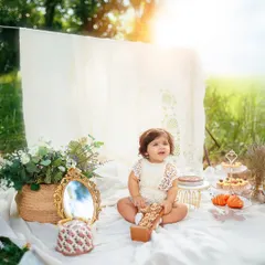 A wider view of the whimsical outdoor first birthday setup, complete with a tiered dessert stand, flowers, and a beautiful lace backdrop.