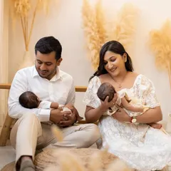 A beautiful family moment with newborn twins. The parents are seated on the floor of my boho-themed studio, each holding one of their babies and looking down with adoration.