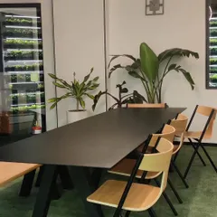 This simple and clean meeting area features a large table and ergonomic chairs, set against a backdrop of indoor plants. It's a functional space designed for team collaboration.