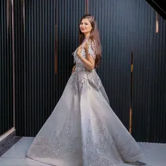 A side profile of the silver ball gown, highlighting the delicate feather-like details on the shoulders and the shimmering fabric. It's a true showstopper available for rent.