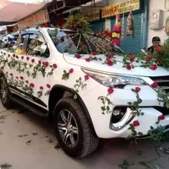 A beautiful wedding car decoration for a white SUV. The design features climbing vines of red roses, creating a romantic and eye-catching look.
