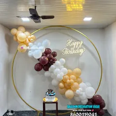 This minimalist and chic birthday backdrop features a simple gold ring with a cascade of balloons in neutral and maroon tones. A small stand is included for the birthday cake.