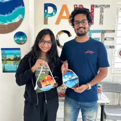 A couple proudly holds up the matching canvas paintings they created in our studio.