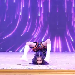 A young performer takes center stage, demonstrating advanced flexibility with a chest stand. Our training helps students of all ages build the confidence to perform solo in front of a large audience.