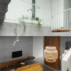 The living area is defined by its raw, minimalist material palette, including an exposed concrete feature wall and ceiling. The yellow sofa adds a vibrant splash of color to the neutral space.