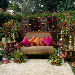 A vibrant Mehandi ki Mehfil, styled for a modern celebration while honoring tradition. This outdoor setup features a beautiful carved wooden screen, marigold garlands, and plush seating in jewel tones, creating the perfect backdrop for photos and festivities.