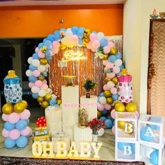 A "He or She" gender reveal or baby shower theme. This setup uses a pink and blue balloon arch, 'OH BABY' light-up letters, and baby bottle foil balloons to create a fun and festive atmosphere.