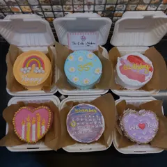 To show the range of bento designs, here is a hamper of six different cakes. Each one has a unique, hand-painted design, including a rainbow, a calendar month, and floral patterns, perfect for assorted gifting.