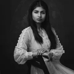 A classic black and white portrait of a "muse" in a delicate lace dress. The dark background and soft lighting create a timeless, painterly feel.