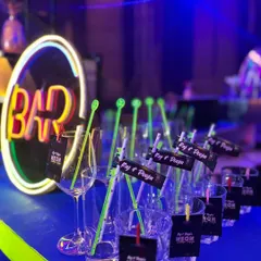 A vibrant neon-themed bar setup, complete with a glowing 'BAR' sign and personalized drink tags for 'Raj & Pooja's Neon Night'.