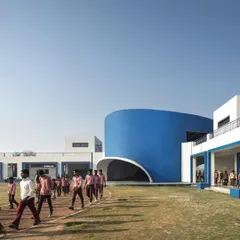 The school's campus features a bold, curved blue volume that houses an amphitheater, creating a dynamic focal point for student activity.