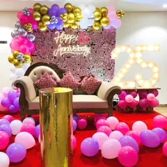 A luxurious 25th anniversary decoration in pink, purple, and gold. This setup includes a comfortable couch for photos, set against a sequin backdrop and framed by a balloon garland and light-up '25'.