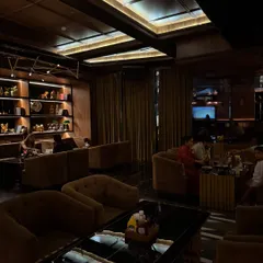 The interior of LimitlessLuxe in Noida showcases a moody and sophisticated ambiance. The dark wood tones, plush velvet seating, and strategic recessed lighting create an exclusive and comfortable lounge experience, perfect for a high-end dine-in spot.