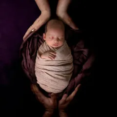 A powerful photo showing a swaddled newborn held securely in the hands of their parents.