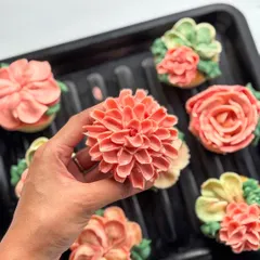 This coral-pink dahlia cupcake shows the intricate layers of petals I pipe for a realistic look.