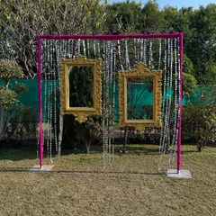 A creative outdoor photo booth I designed. It features two ornate golden frames hanging from a structure against a backdrop of shimmery strings, perfect for guest photos.