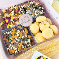 This assorted treat box is perfect for sharing. It includes a mix of my popular items: chocolate bark with nuts, rose-petal bark, Biscoff bark, and nankhatai cookies, with a "Happy Rakhi" tag.