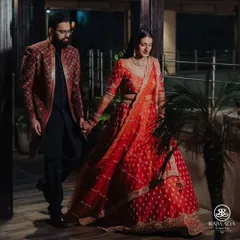 A stunning couple walking hand-in-hand. Our client looks dashing in a deep red and black embroidered Indo-Western outfit, perfectly complementing his bride's lehenga for their reception.