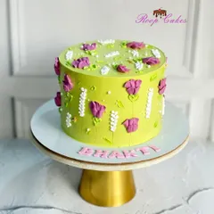 Bursting with color and life, this cake features vibrant green frosting and is decorated with beautiful purple and white flowers created with a palette knife.