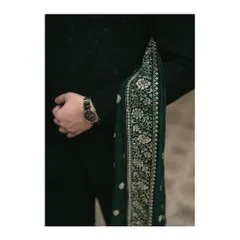 A close-up of the groom's attire, showing the rich texture of his black sherwani and the intricate embroidery on the green sash. A classic watch adds a touch of modern elegance.