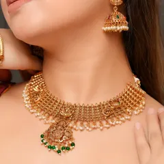 A focused shot on a traditional gold choker necklace with a temple jewelry pendant. The image clearly displays the texture of the gold and the fine details of the design.