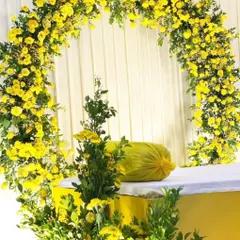 A simple and bright Haldi backdrop, featuring a floral arch made entirely of yellow flowers, perfect for intimate home ceremonies.