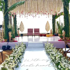 We designed this beautiful beach wedding aisle with a custom message that reads 'With my whole heart, for my whole life'. The walkway leads to a traditional stage framed by banana leaves and hanging tuberose garlands, blending coastal charm with classic elegance.