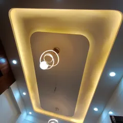 A finished false ceiling with a simple rectangular design and cove lighting. The hanging decorative light adds a final touch of elegance.