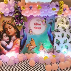 A Krishna themed baby shower (Seemant Sanskar) decor. The backdrop features a beautiful image of Yashoda and Krishna, peacock feather motifs, and an 'Oh Baby' neon sign, all framed by a pastel balloon arch.