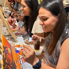 A participant enjoying a drink while adding the finishing touches to her sunset painting. This is what sip and paint is all about: relaxing, creating, and having fun.
