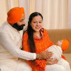 A portrait of a Sikh couple with their newborn, radiating peace and joy. The vibrant orange of their traditional clothing adds a beautiful warmth to this sacred family moment.