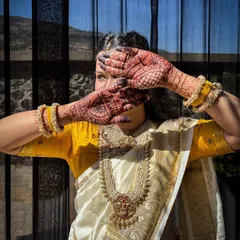 Another artistic shot of the bride, with her henna-stained hands partially covering her face. The sunlight highlights the rich, deep color of the mehendi.