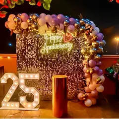 An outdoor terrace setup for a 25th anniversary. This design features a silver sequin wall that sparkles at night, a balloon arch in purple and gold, and large '25' marquee numbers.