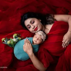 A dramatic and artistic portrait of a mother and her newborn. The vibrant red fabric creates a stunning visual contrast, enveloping them in a sea of color while highlighting their serene connection.