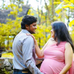 A candid moment between a couple during their outdoor maternity shoot. The natural light and green surroundings create a warm and peaceful atmosphere.