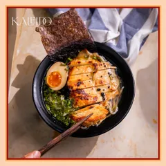 A close-up of our comforting chicken ramen bowl. Notice the perfectly seared chicken, the rich jammy egg, fresh greens, and a sheet of nori, all swimming in a deeply flavorful broth.