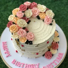 A beautiful birthday cake with a cascade of hand-piped buttercream roses in a warm, sunset-inspired color palette.