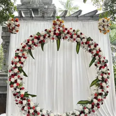 This circular floral arch is one of our most popular designs for receptions and engagements. It creates a stunning photo backdrop using a mix of red, white, and orange flowers, blending modern style with traditional elements.