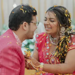 A bride and groom share a laugh while being covered in flower petals during their Haldi. We focus on the couple's interaction and shared joy.