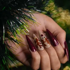 Another perspective of the reindeer nail set, showcasing the length and dramatic shape of the stiletto extensions against a festive green background.