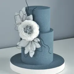 A pretty two-tiered blue cake with a glitter finish and a large, handcrafted white wafer paper flower.
