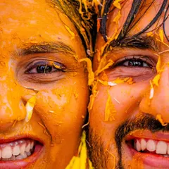 A super close-up shot capturing the happy, turmeric-covered faces of the bride and groom. This image is all about the texture, the vibrant color, and the infectious smiles.