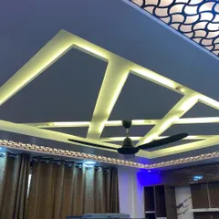 A dramatic false ceiling design with geometric patterns and multiple layers of lighting. The central section features a laser-cut jaali panel that is backlit for a stunning effect.